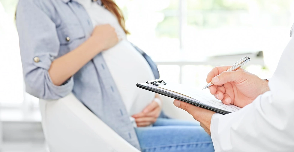 Arzt notiert Informationen während Beratung mit schwangerer Frau